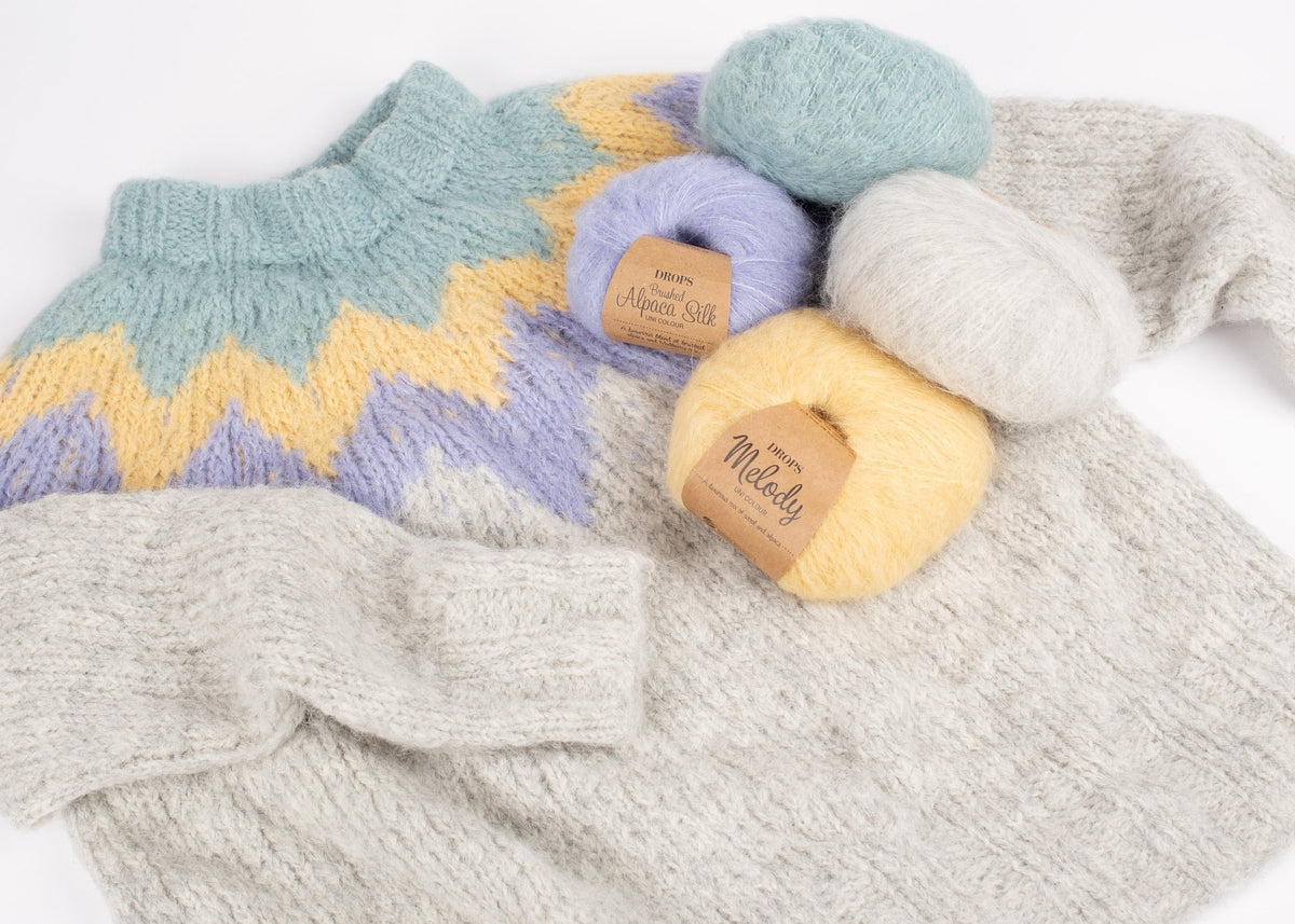 Nystan av DROPS Brushed Alpaca Silk och DROPS Melody ovanpå en handstickad tröja i grått, gult och lila